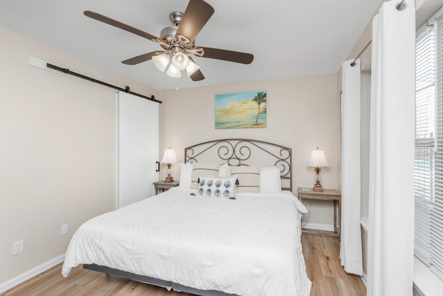 bedroom with a barn door, light wood-style flooring, and baseboards