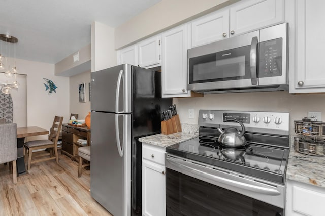 kitchen with appliances with stainless steel finishes, white cabinets, light wood-style floors, and light stone countertops