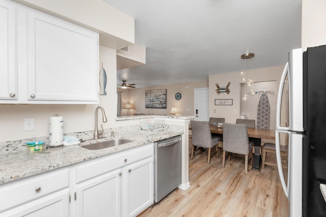 kitchen featuring decorative light fixtures, stainless steel dishwasher, freestanding refrigerator, white cabinets, and a sink