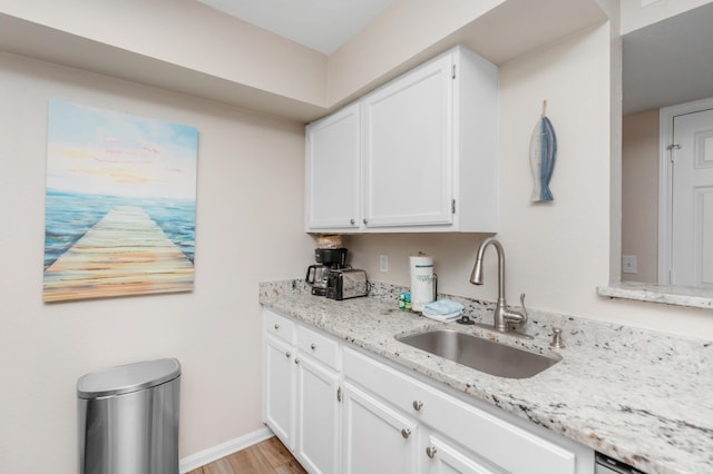 kitchen featuring baseboards, white cabinets, light stone counters, light wood-style floors, and a sink