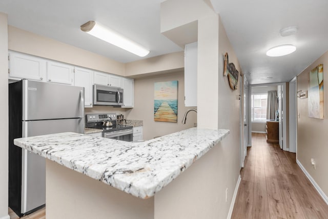 kitchen featuring stainless steel appliances, light wood-style flooring, white cabinets, a peninsula, and baseboards