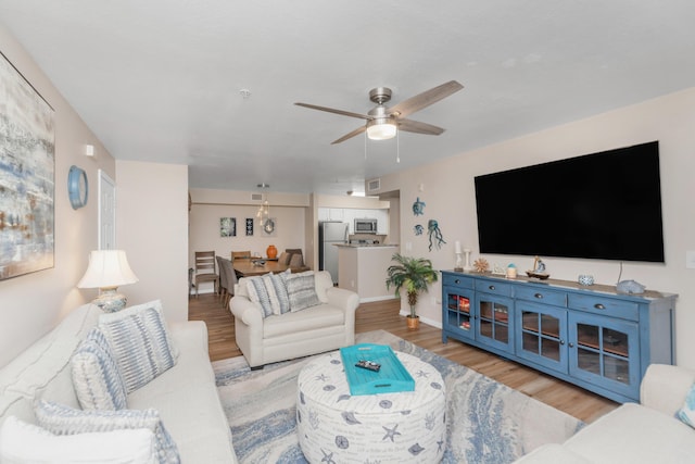 living room featuring ceiling fan, light wood finished floors, and baseboards