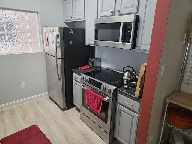 kitchen with stainless steel appliances, baseboards, white cabinets, light wood-style floors, and dark countertops