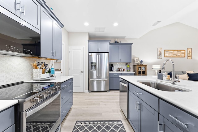 kitchen featuring light wood-style flooring, appliances with stainless steel finishes, vaulted ceiling, light countertops, and a sink