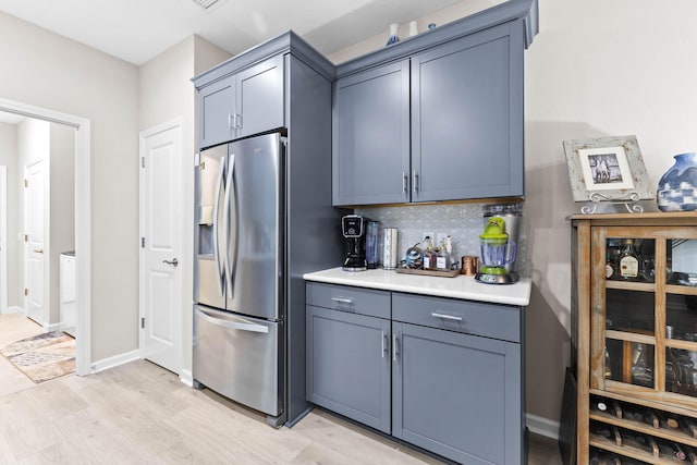 kitchen featuring tasteful backsplash, light countertops, light wood-type flooring, stainless steel fridge, and baseboards