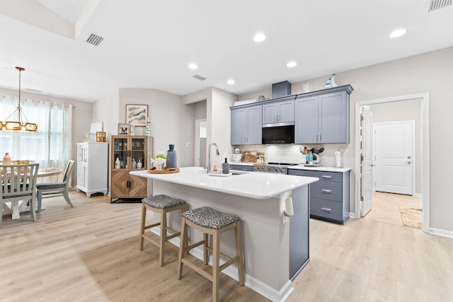 kitchen featuring light wood-style flooring, a sink, light countertops, hanging light fixtures, and a center island with sink