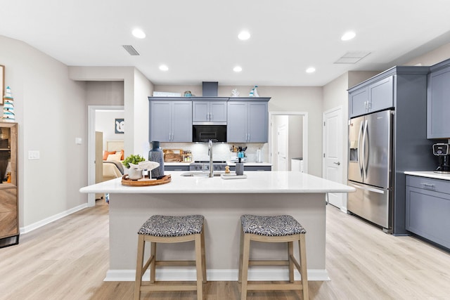 kitchen with light countertops, a breakfast bar area, stainless steel fridge, and a kitchen island with sink