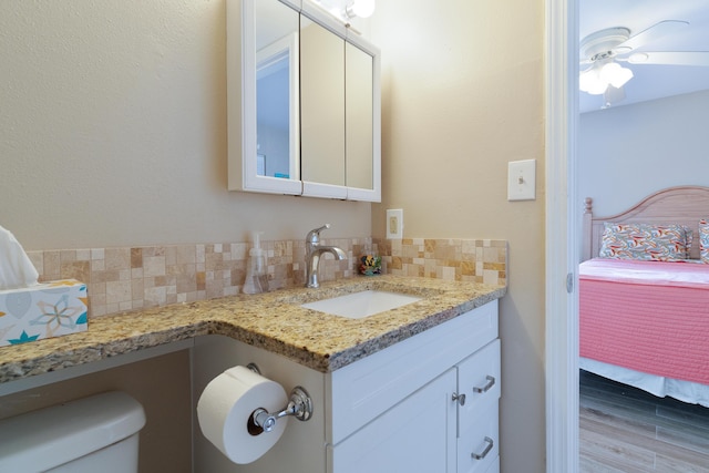 ensuite bathroom with decorative backsplash, toilet, ceiling fan, vanity, and ensuite bath