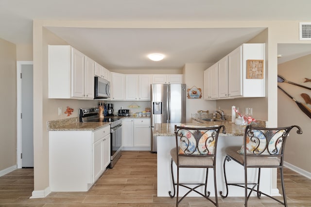 kitchen featuring light stone counters, white cabinetry, a kitchen breakfast bar, appliances with stainless steel finishes, and light wood-type flooring