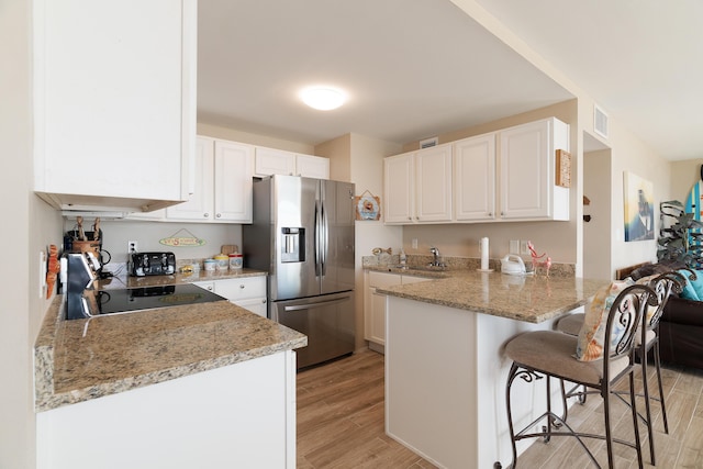 kitchen with a peninsula, light stone counters, stainless steel refrigerator with ice dispenser, and white cabinetry