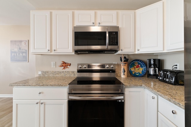 kitchen featuring stainless steel appliances, light stone counters, light wood-style flooring, and white cabinets