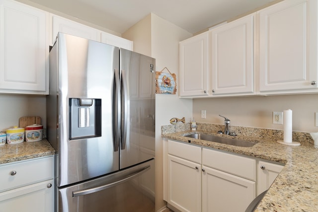 kitchen featuring white cabinets, stainless steel fridge, a sink, and light stone countertops