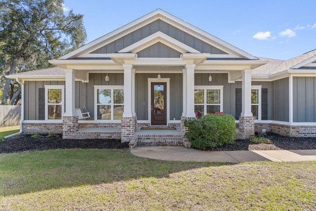 view of front of house featuring a shingled roof, covered porch, a front lawn, board and batten siding, and brick siding