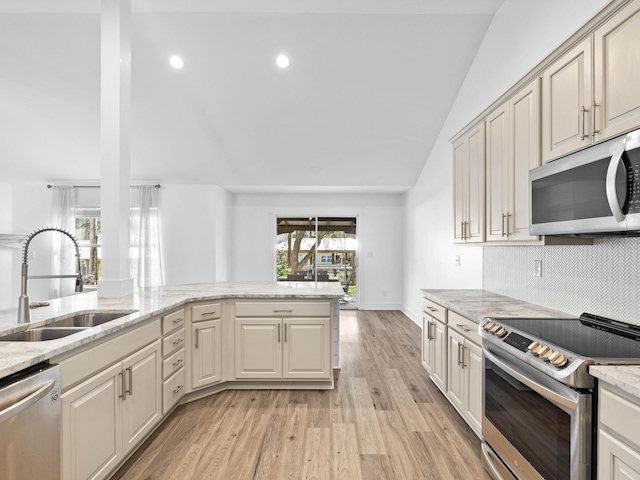 kitchen with lofted ceiling, light wood-style flooring, stainless steel appliances, a sink, and light stone countertops