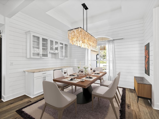 dining area with dark wood-style floors, a raised ceiling, a chandelier, and wooden walls