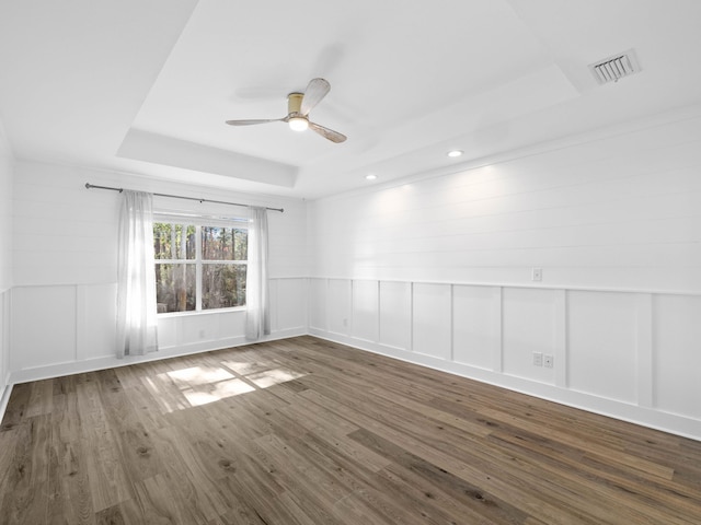 unfurnished room with dark wood finished floors, a raised ceiling, visible vents, and a decorative wall