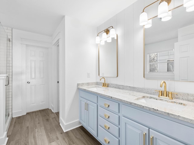 full bath with double vanity, a sink, a shower stall, and wood finished floors