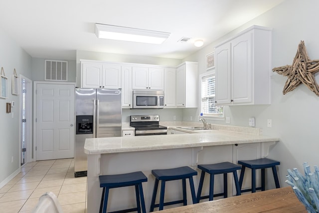 kitchen featuring a sink, visible vents, a kitchen breakfast bar, white cabinetry, and appliances with stainless steel finishes