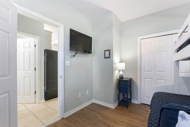 bedroom featuring light wood-style floors, freestanding refrigerator, a closet, and baseboards