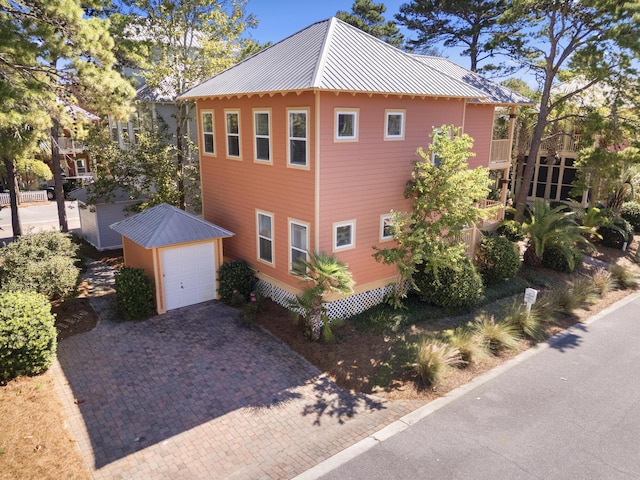 view of home's exterior with a garage, metal roof, decorative driveway, and an outdoor structure