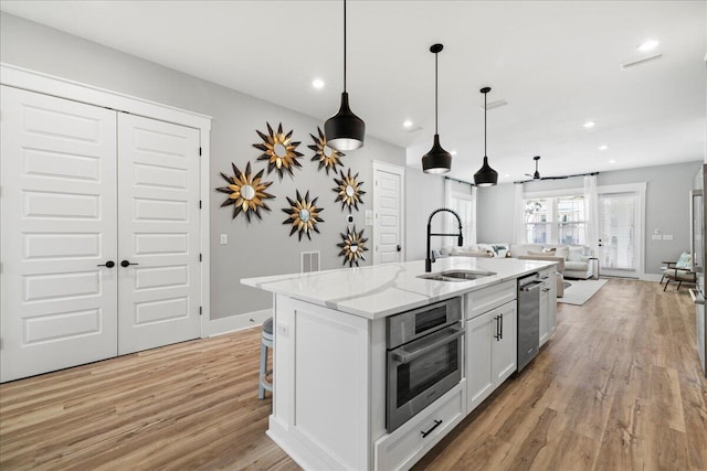 kitchen with light wood-style flooring, appliances with stainless steel finishes, open floor plan, a kitchen island with sink, and a sink