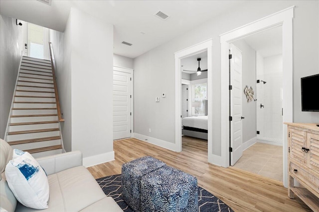 living room featuring stairs, light wood-type flooring, visible vents, and baseboards