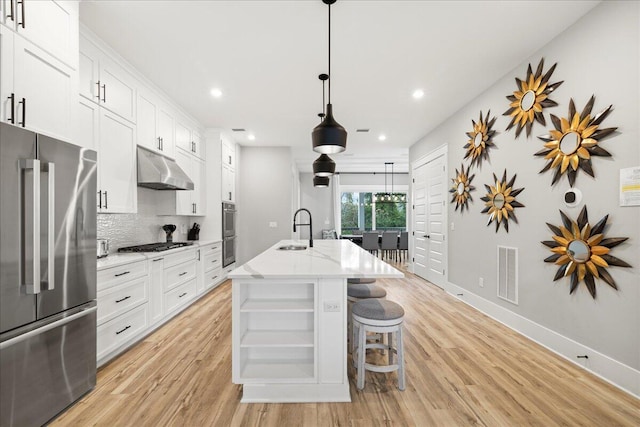 kitchen featuring under cabinet range hood, a sink, visible vents, appliances with stainless steel finishes, and a center island with sink