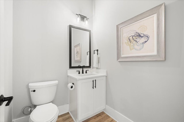 half bathroom with wood finished floors, vanity, toilet, and baseboards