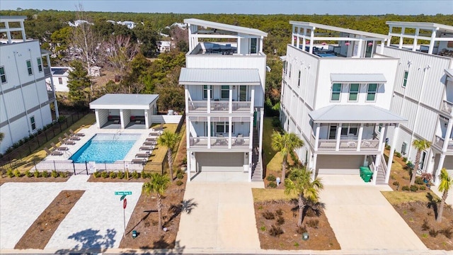 rear view of property featuring a garage, driveway, stairs, fence, and a community pool