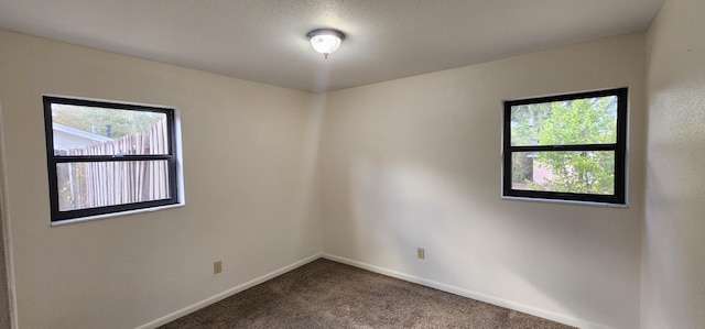 empty room featuring dark colored carpet, plenty of natural light, and baseboards