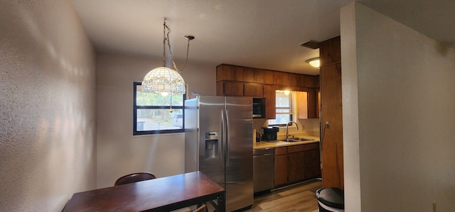 kitchen featuring stainless steel appliances, a sink, light countertops, light wood-type flooring, and brown cabinetry