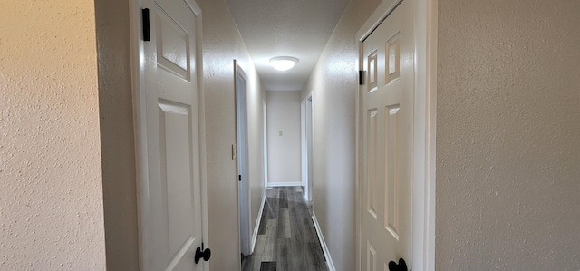 hallway featuring dark wood-type flooring, a textured wall, and a textured ceiling