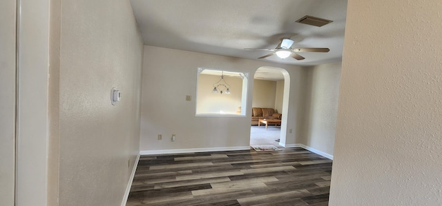 unfurnished room with visible vents, arched walkways, baseboards, dark wood-style floors, and ceiling fan