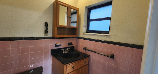 half bath with toilet, a textured wall, vanity, and tile walls