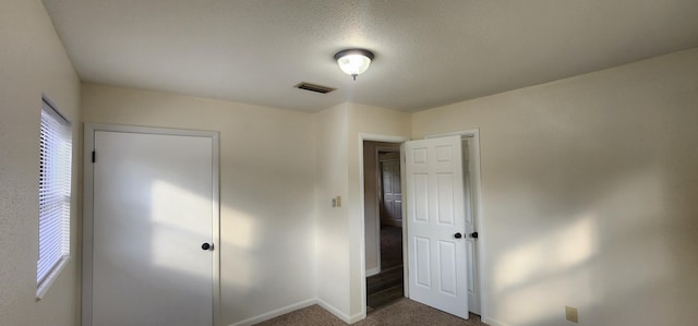 unfurnished bedroom with a textured ceiling, dark colored carpet, visible vents, and baseboards