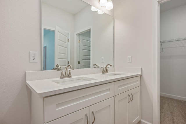 bathroom featuring a sink, baseboards, double vanity, and a spacious closet