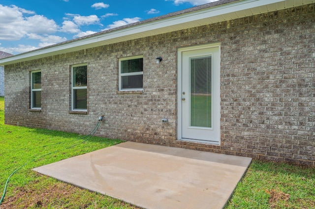 rear view of house featuring a lawn, brick siding, and a patio area