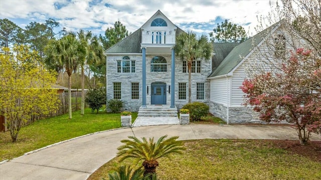 view of front facade featuring stone siding, fence, and a front yard