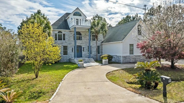 view of front of home featuring a front yard, stone siding, driveway, and a balcony