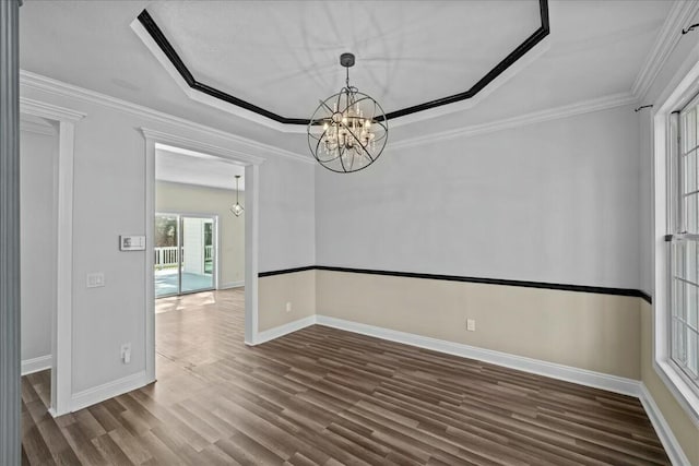 spare room with a notable chandelier, ornamental molding, a raised ceiling, and wood finished floors