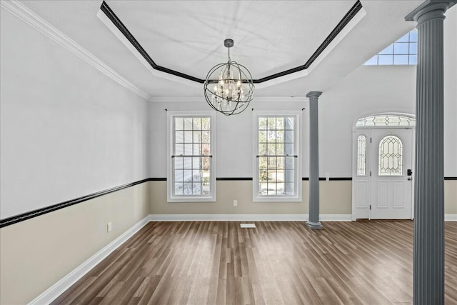 interior space featuring a raised ceiling, a notable chandelier, decorative columns, and wood finished floors