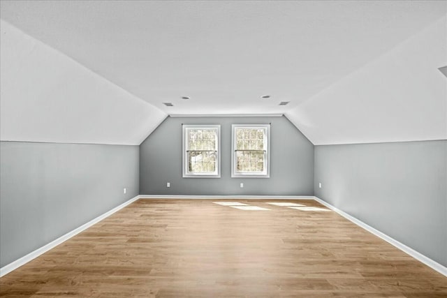 additional living space with light wood finished floors, visible vents, baseboards, and vaulted ceiling