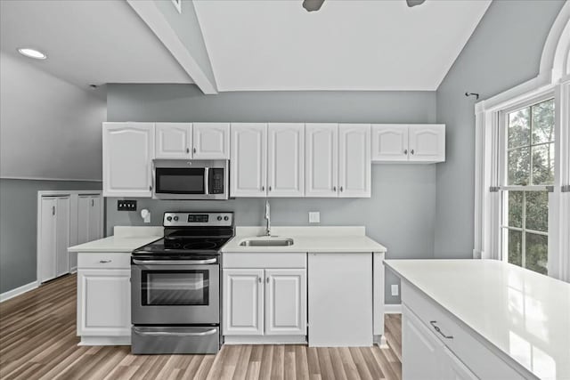 kitchen featuring appliances with stainless steel finishes, lofted ceiling, white cabinetry, and a sink