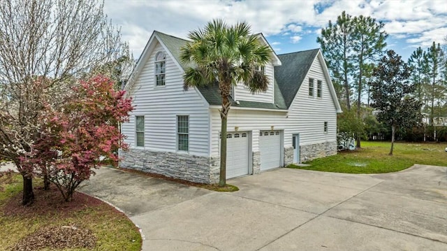 view of side of home featuring driveway, stone siding, a shingled roof, and a lawn