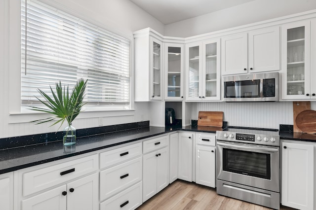 kitchen featuring appliances with stainless steel finishes, dark countertops, light wood-style flooring, and white cabinets