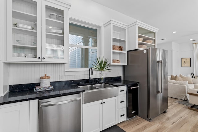 kitchen featuring light wood-style flooring, stainless steel appliances, a sink, open shelves, and glass insert cabinets