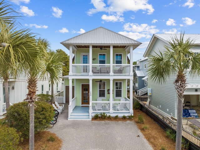 coastal home with a ceiling fan, a balcony, metal roof, covered porch, and fence