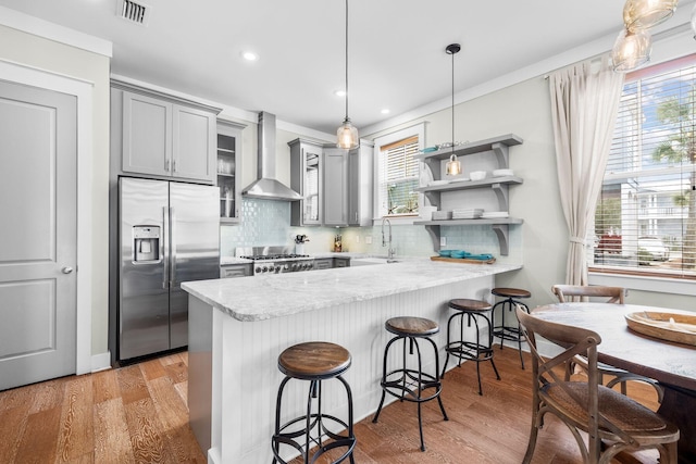 kitchen with gray cabinets, visible vents, stainless steel fridge, a peninsula, and wall chimney exhaust hood