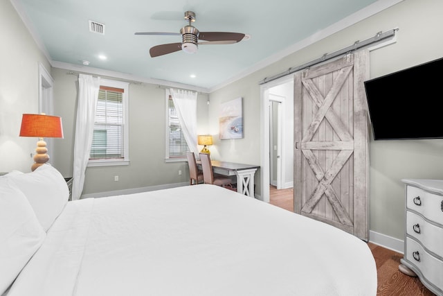 bedroom with a barn door, baseboards, visible vents, ornamental molding, and wood finished floors