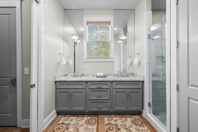 full bathroom featuring double vanity, wood finished floors, a stall shower, and a sink